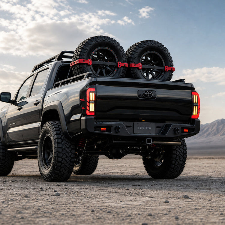 Low rear view of smoked LED tail lights for 2016-2023 Toyota Tacoma on a black truck carrying two spare tires.
