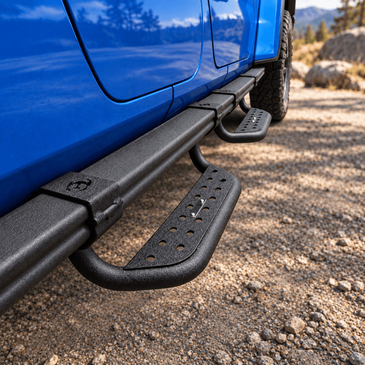 Two black side steps installed along the rock rail of a blue Jeep Gladiator JT, viewed at an angle.