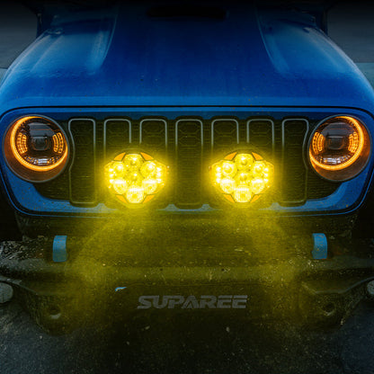 Two SUPAREE HELM 7 LED pod lights shining amber light from the front bumper of a blue Jeep.