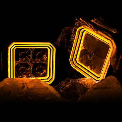 Pair of SUPAREE HYPER 5 RGBW LED pod lights with amber backlighting on rocks.
