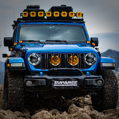Blue Jeep on a rocky trail with two amber-covered SUPAREE HELM 7 off-road lights on its front bumper.