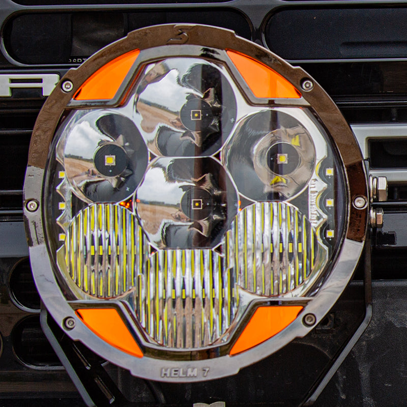 Front view of a SUPAREE HELM 7 round LED driving light showing its clear lens, reflectors and amber DRL sections.