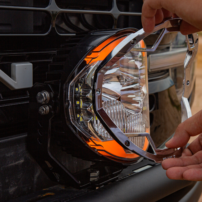Hands removing the front bezel from a SUPAREE HELM 7 LED driving light mounted on a vehicle bumper.