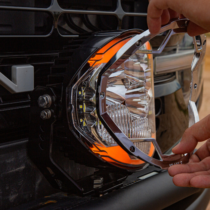 Hands removing the front bezel from a SUPAREE HELM 7 LED driving light mounted on a vehicle bumper.