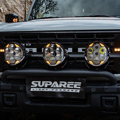 Three round SUPAREE HELM 7 off-road lights mounted across the front bumper of a Ford Bronco.