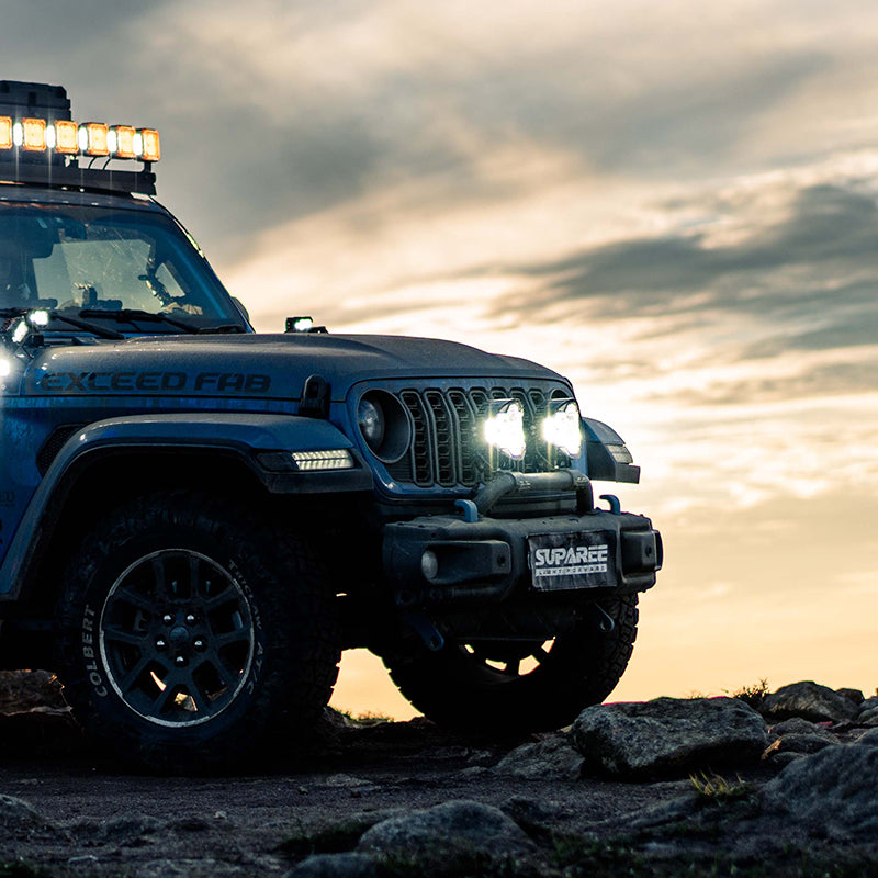SUPAREE HELM 7 LED driving lights shining white light from a blue Jeep on rocks beneath an evening sky.