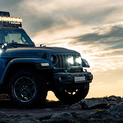 SUPAREE HELM 7 LED driving lights shining white light from a blue Jeep on rocks beneath an evening sky.