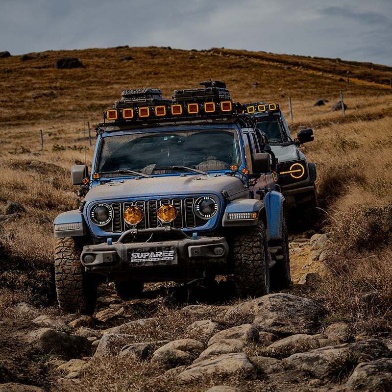 Jeep leading an off-road convoy on a rocky grassland trail with two amber-covered SUPAREE HELM 7 lights on its bumper.