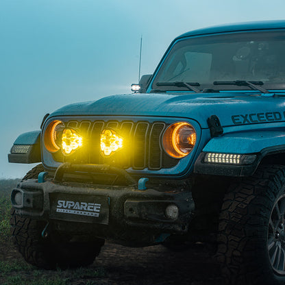 SUPAREE HELM 7 LED driving lights glowing amber on the front bumper of a blue Jeep in mist.