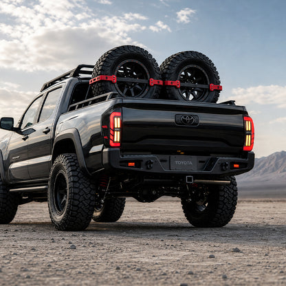 Low rear view of smoked LED tail lights for 2016-2023 Toyota Tacoma on a black truck carrying two spare tires.