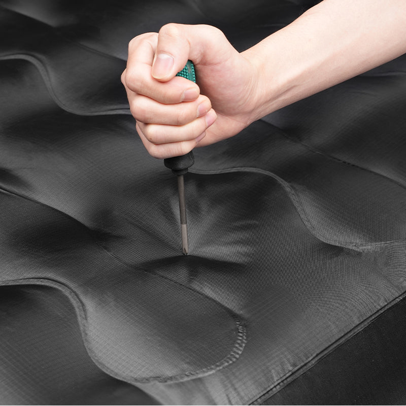 Close-up of a hand pressing a screwdriver into a durable inflatable truck bed air mattress for 2000-2025 Toyota Tundra, showcasing puncture resistance.