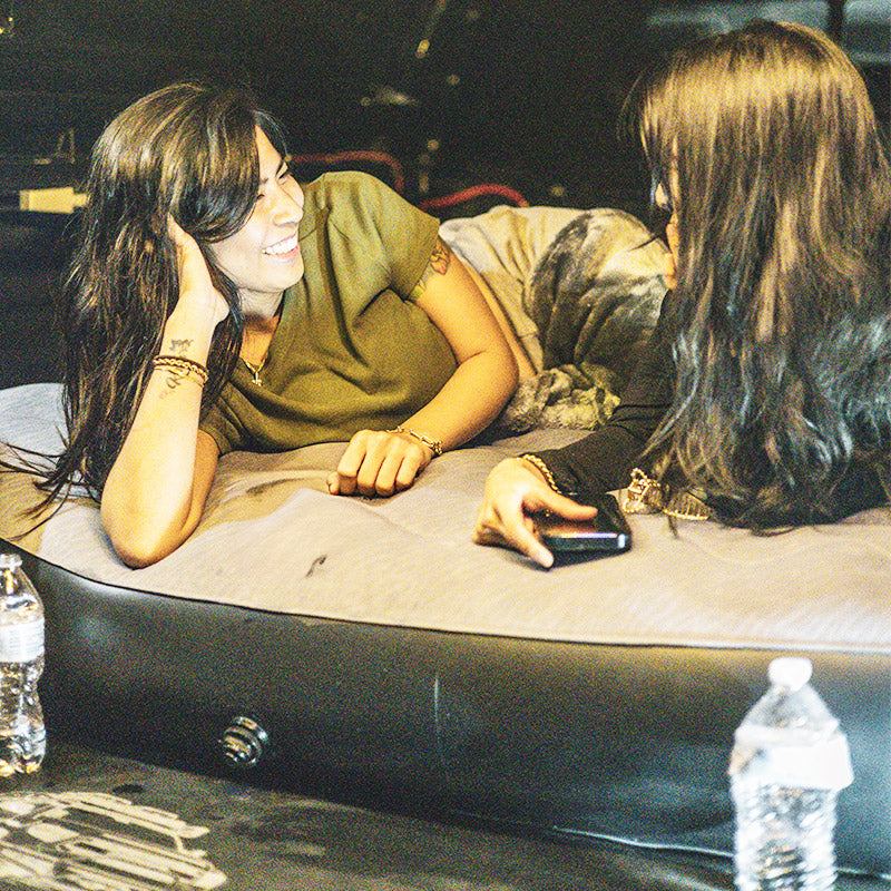 Durable inflatable truck bed air mattress for 2000-2025 Toyota Tundra 5.5FT, shown in use by two women lounging comfortably. Ideal for camping setups.